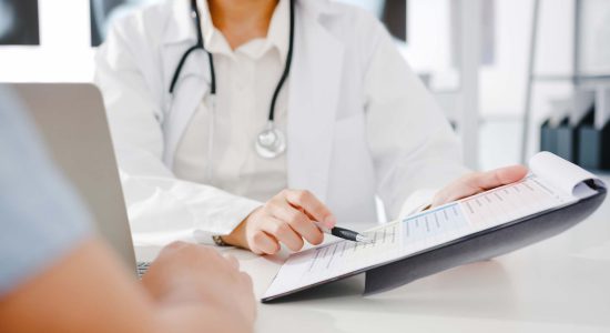 Young Asia female doctor in white medical uniform using clipboard is delivering great news talk discuss results or symptoms with male patient sitting at desk in health clinic or hospital office.